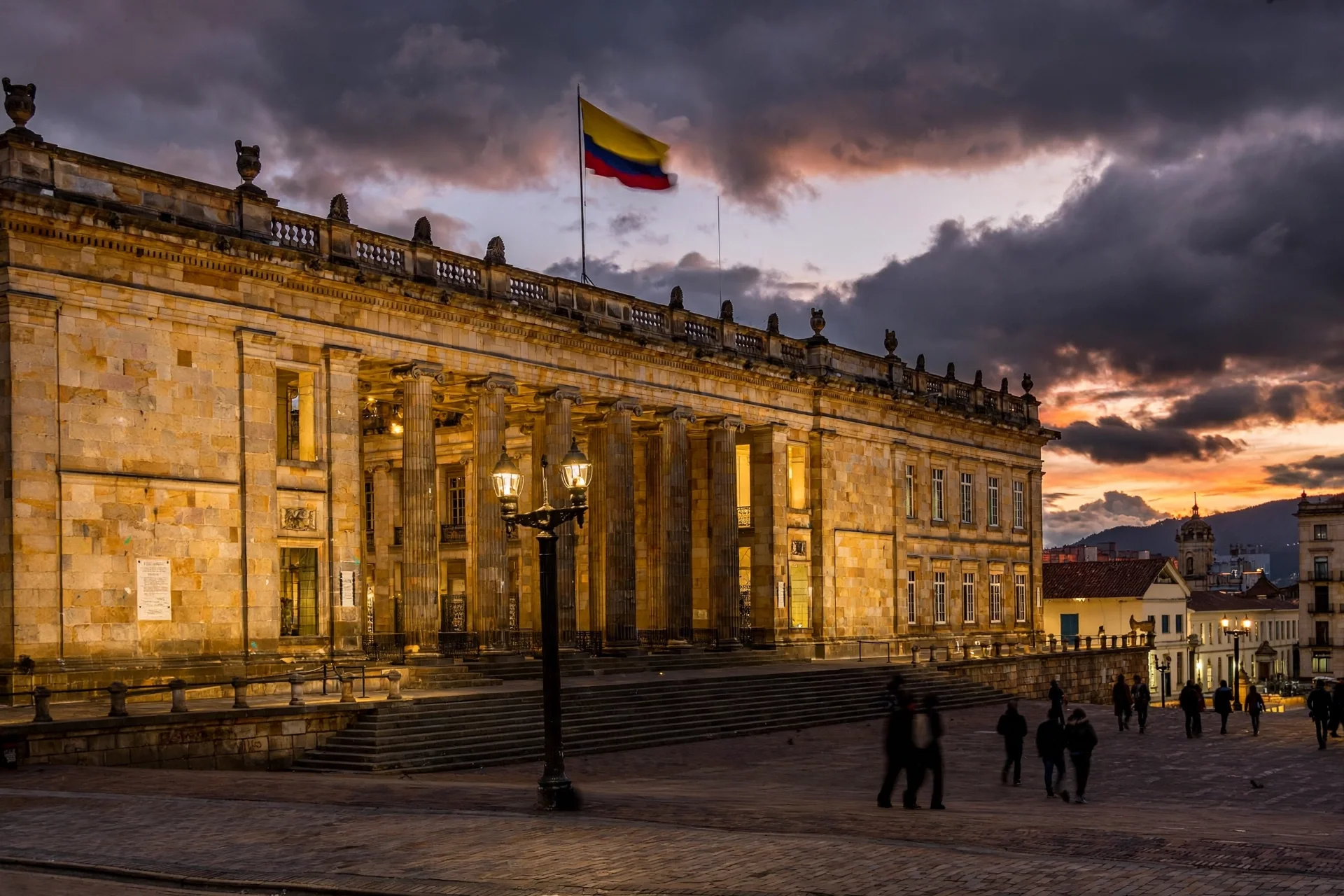 Vista del Capitolio Nacional de Bogotá, sede del Congreso de Colombia, al atardecer, con su fachada neoclásica de piedra iluminada y la bandera colombiana ondeando.