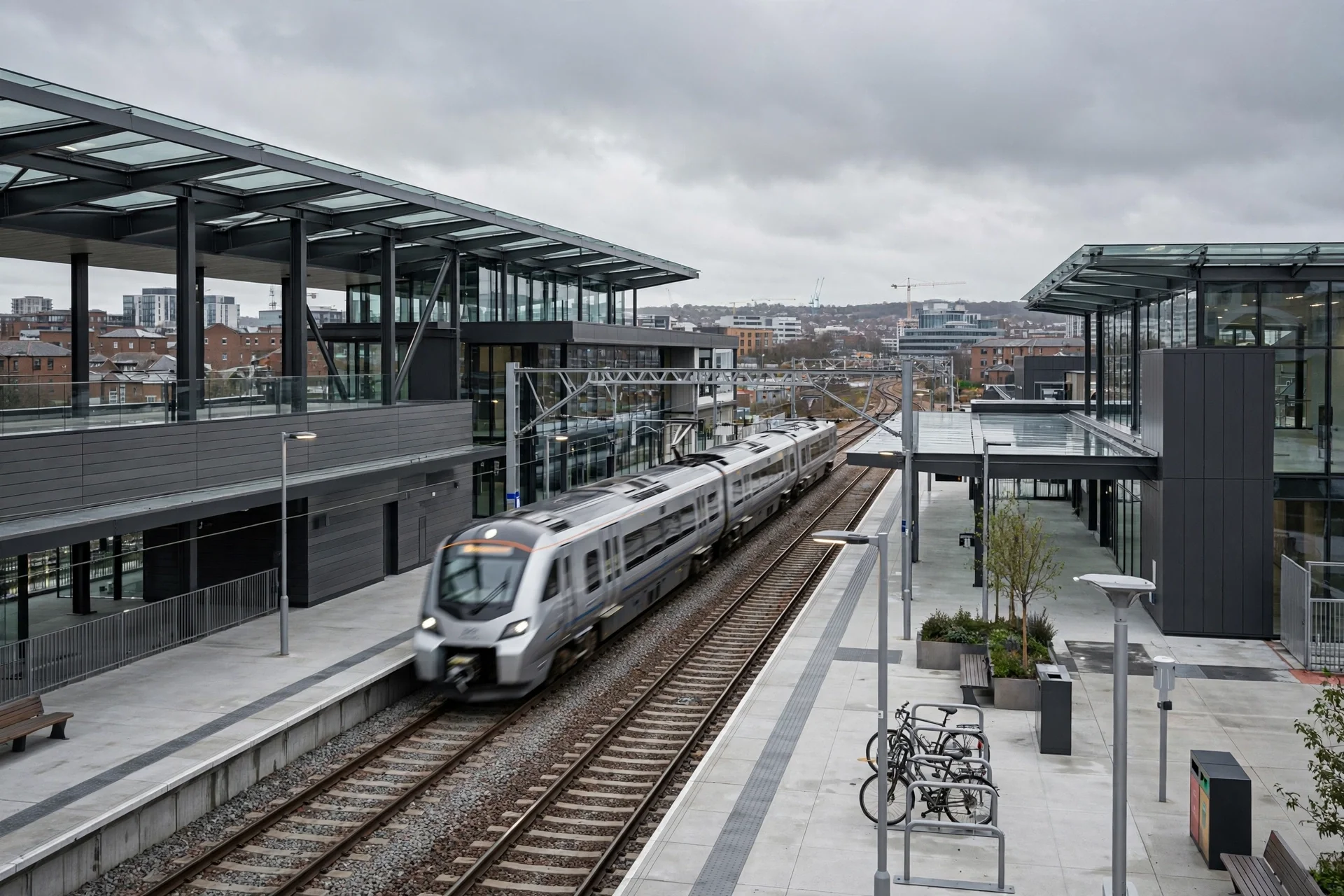 Estación ferroviaria moderna de vidrio y acero con un tren regional plateado llegando al andén y la ciudad al fondo