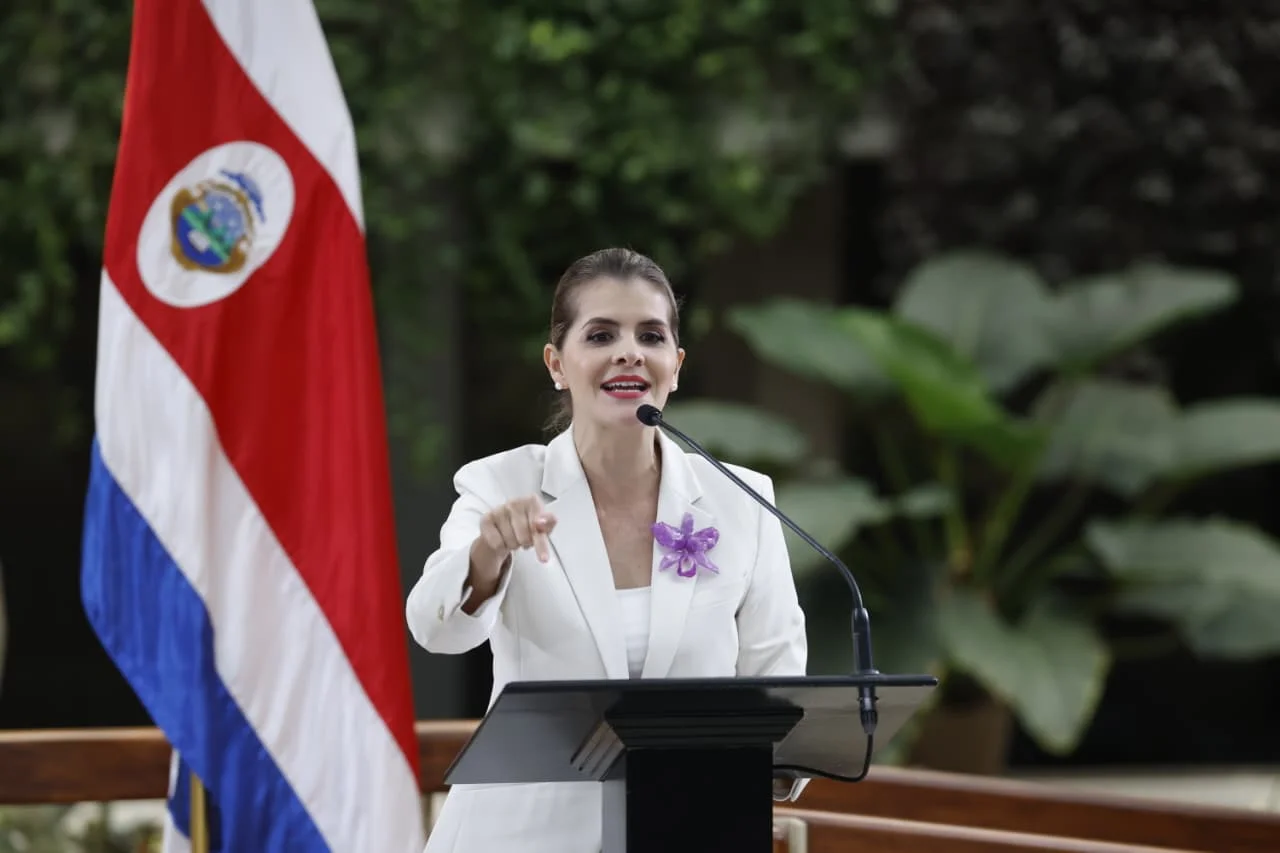 La presidenta de Costa Rica, Laura Fernández, hablando en un atril junto a la bandera costarricense