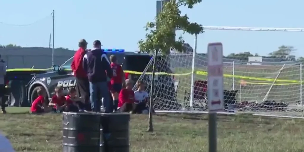 Niños con uniformes rojos junto a un vehículo policial y cinta amarilla en el Stryker Soccer Complex de Wichita, Kansas.