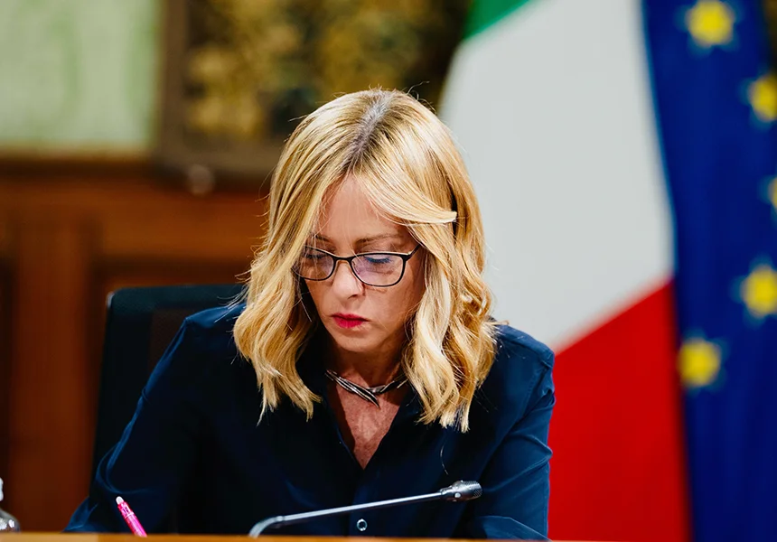 Giorgia Meloni, seated at a desk with the Italian and European Union flags behind her