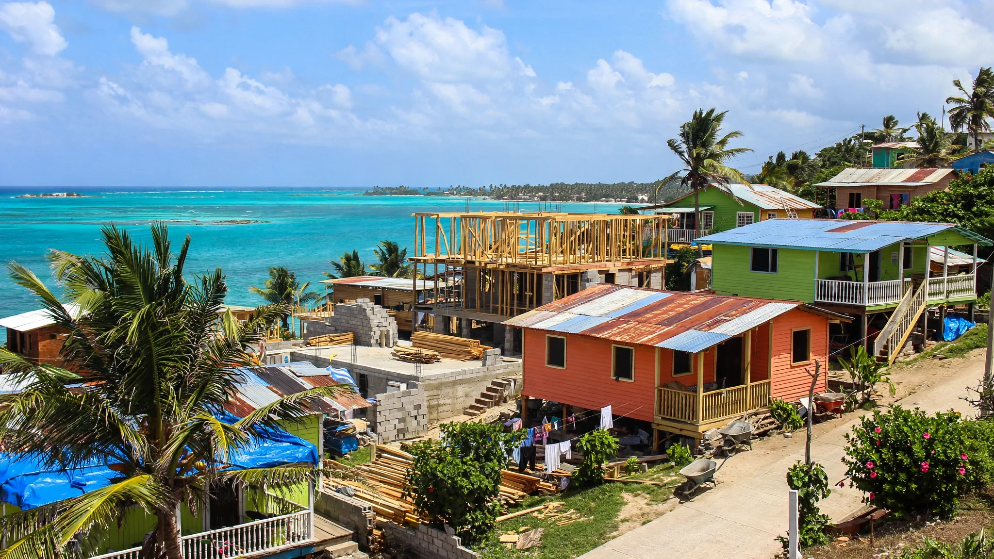 Casas caribeñas de madera de colores en San Andrés, con una vivienda en construcción y el mar turquesa al fondo.