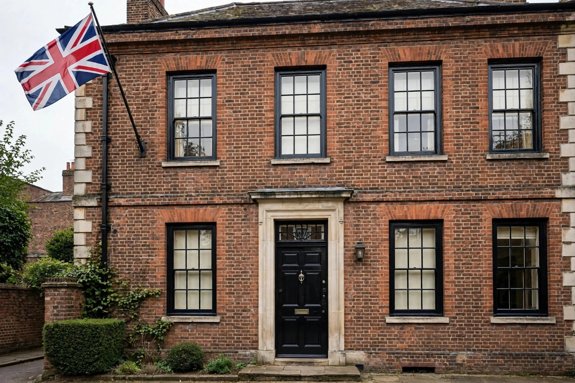 Fachada de ladrillo de una residencia oficial británica con puerta negra y una bandera ondeando, sin personas