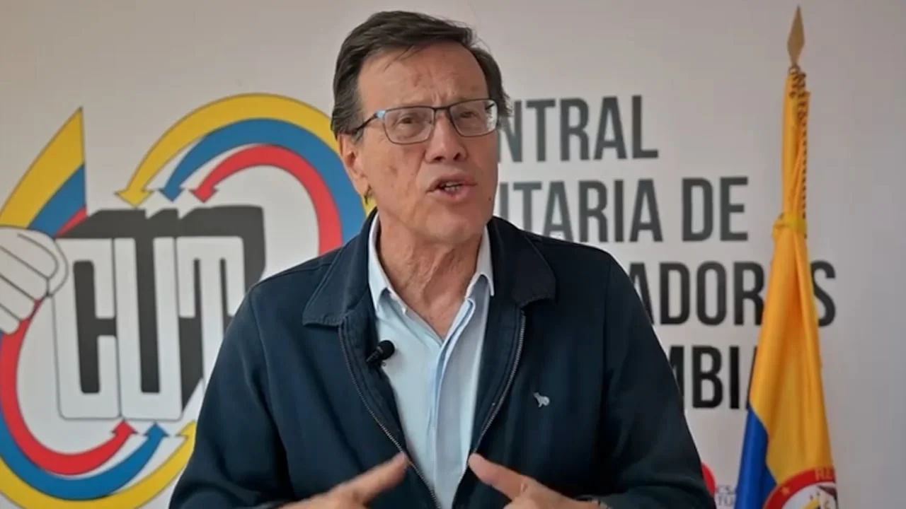 Fabio Arias habla con gestos frente a un fondo con el logo de la CUT y una bandera de Colombia a su lado.