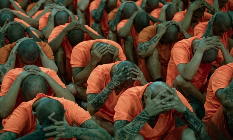Presos con uniformes color naranja y cabezas rapadas, sentados con las manos sobre la cabeza en un pabellón penitenciario