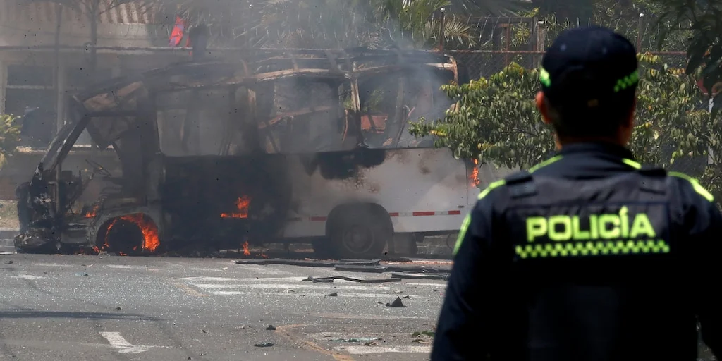 Bus escolar calcinado en una calle de Cali tras el atentado contra el Batallón Pichincha, con un agente de policía en primer plano
