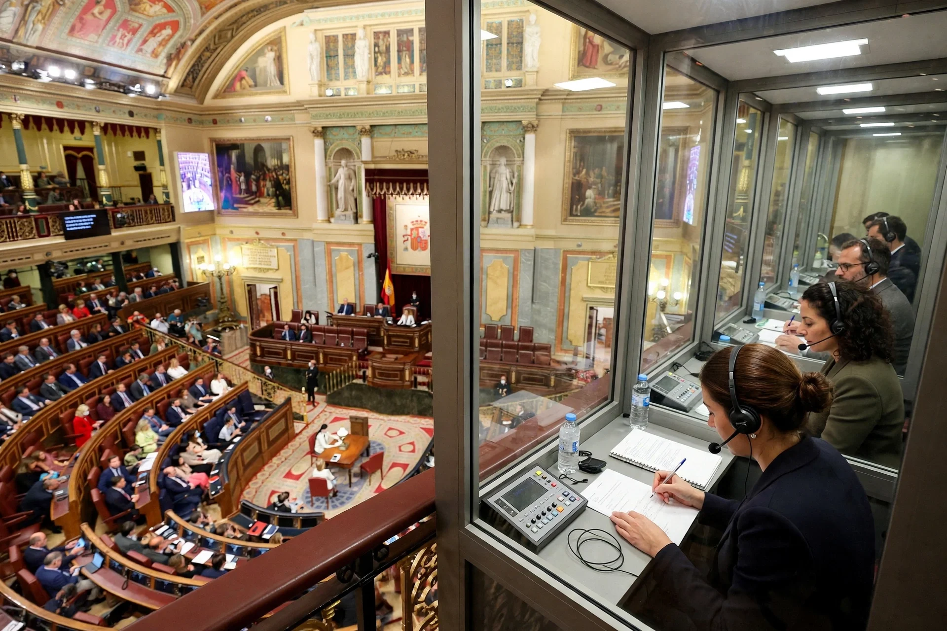 Cámara parlamentaria con senadores e intérpretes con auriculares durante un debate.