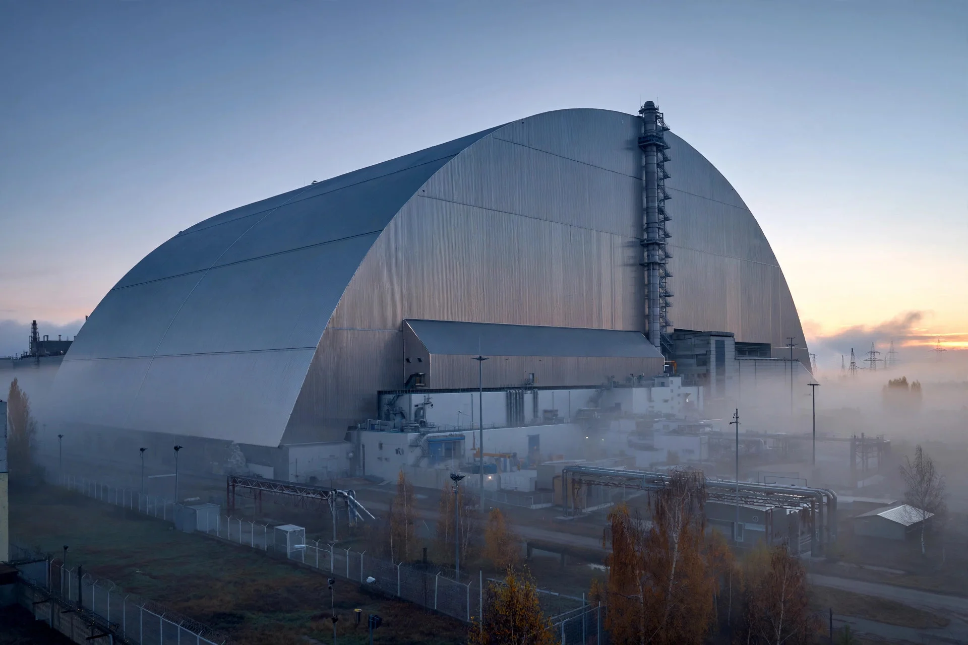 Estructura de confinamiento en arco sobre la planta de Chernóbil al amanecer, entre niebla