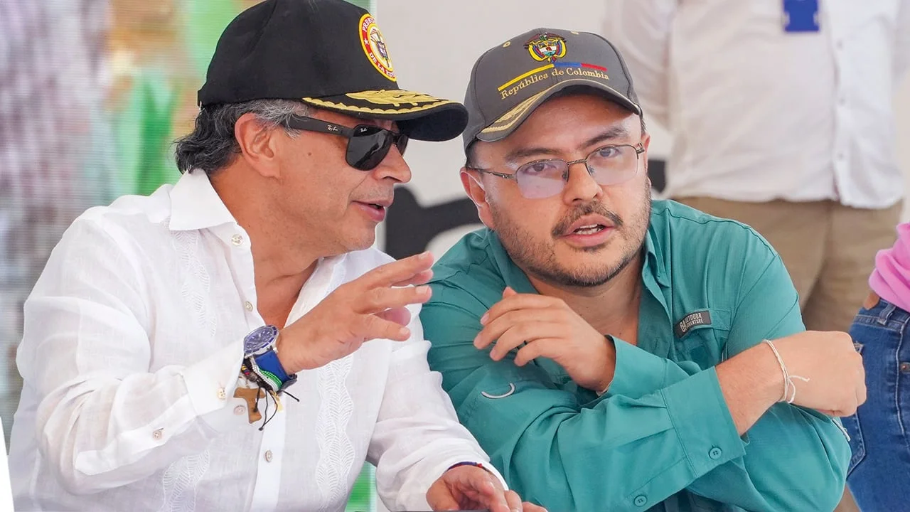 Un hombre con micrófono junto a otro hombre con gorra en un acto público al aire libre en Colombia