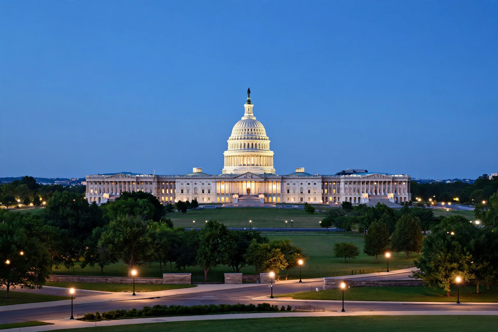 El Capitolio de Estados Unidos iluminado al anochecer, con su cúpula blanca sobre el cielo azul y jardines en primer plano